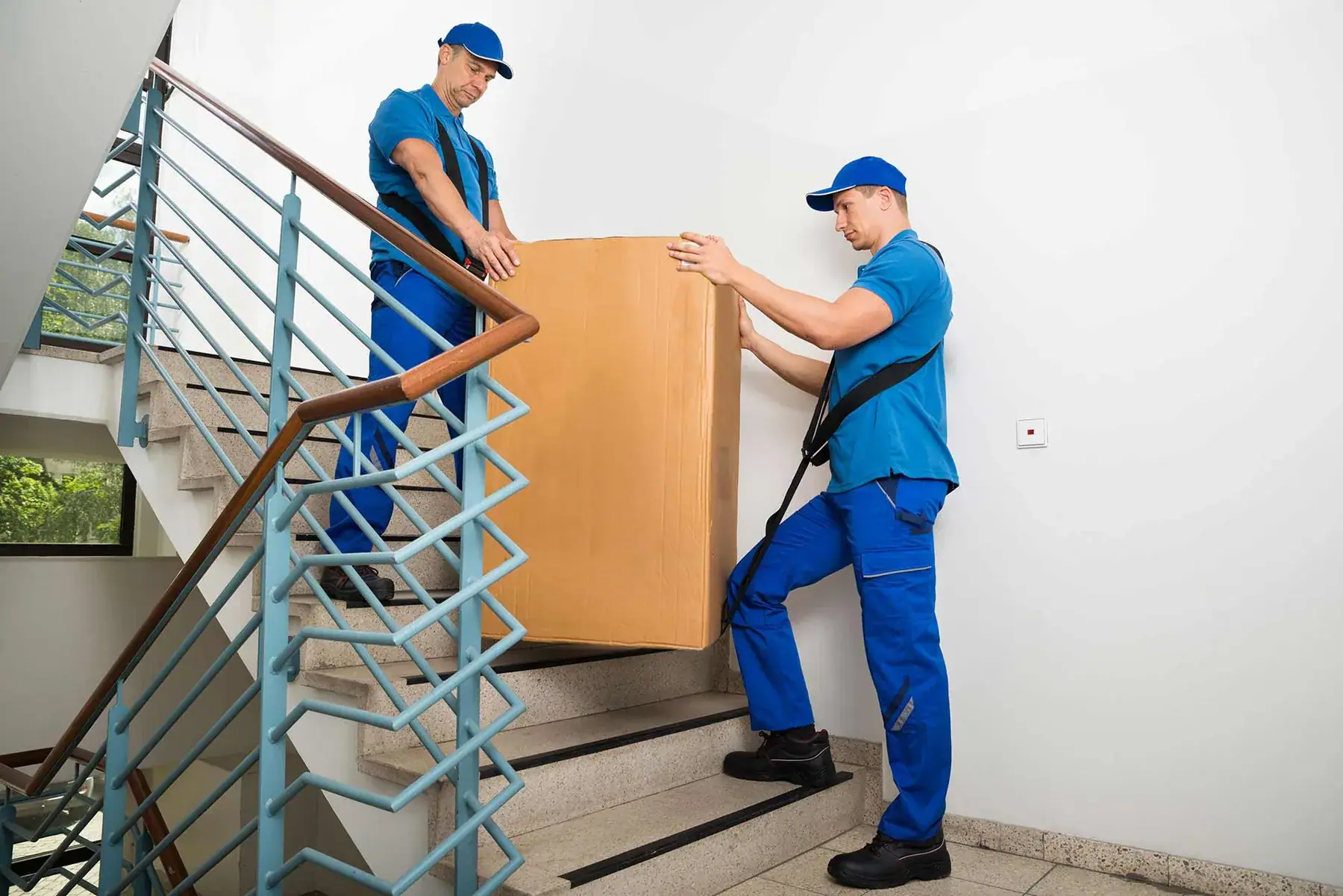 Zwei Möbelpacker tragen einen schweren Gegenstand im Stiegenhaus
